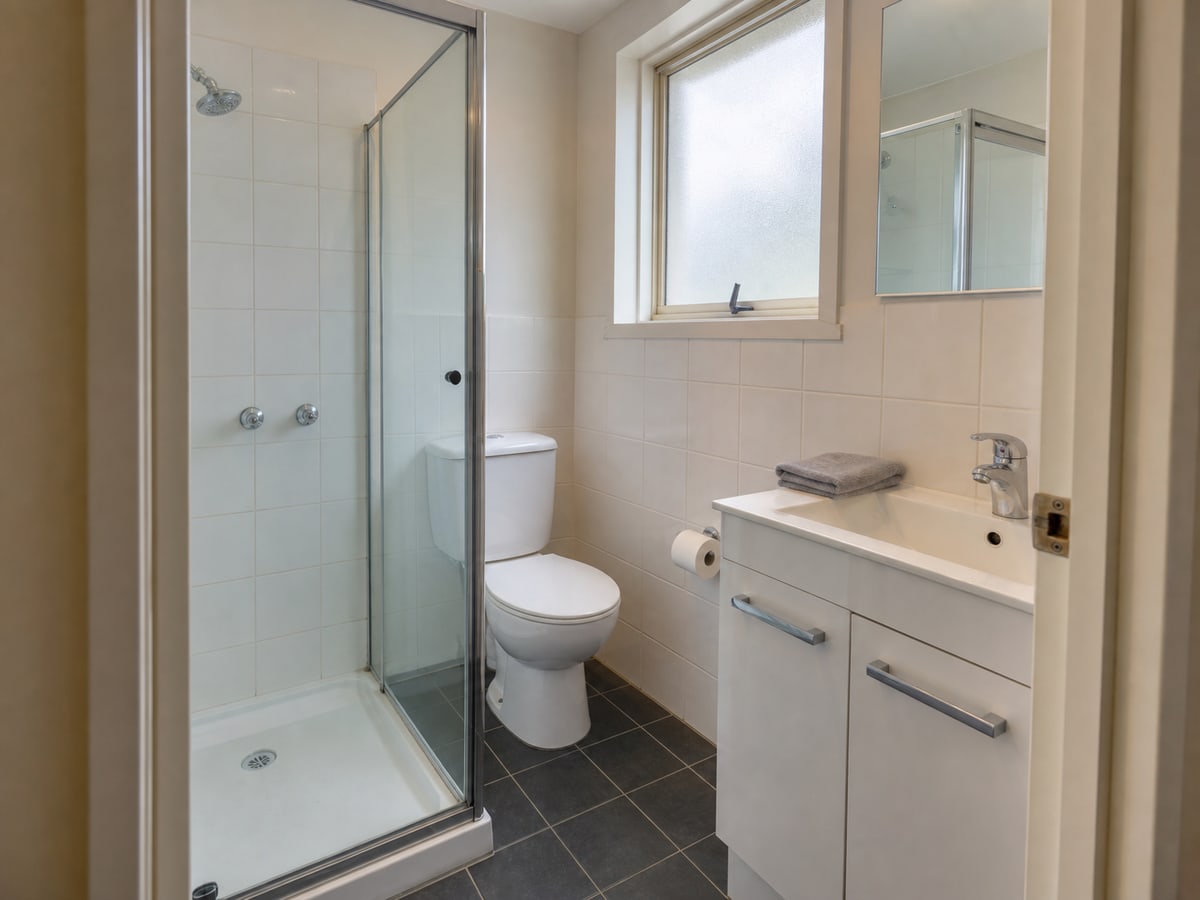 A modest refreshed ensuite with standard white vanity, framed shower and affordable ceramic tiles
